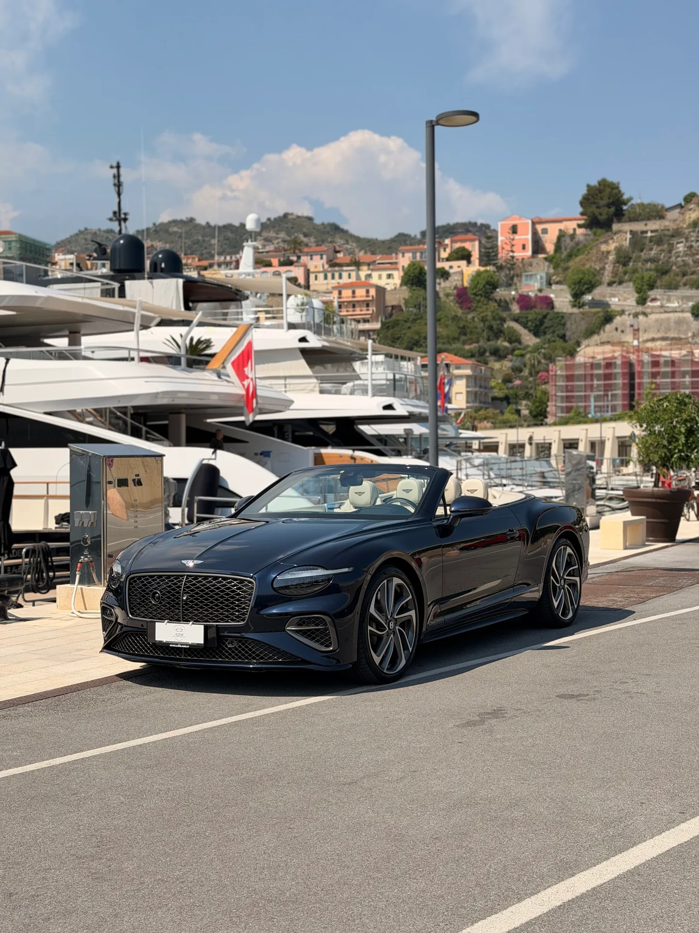 Black Bentley Continental GTC with its roof open, seen from the front three-quarter angle in a marina