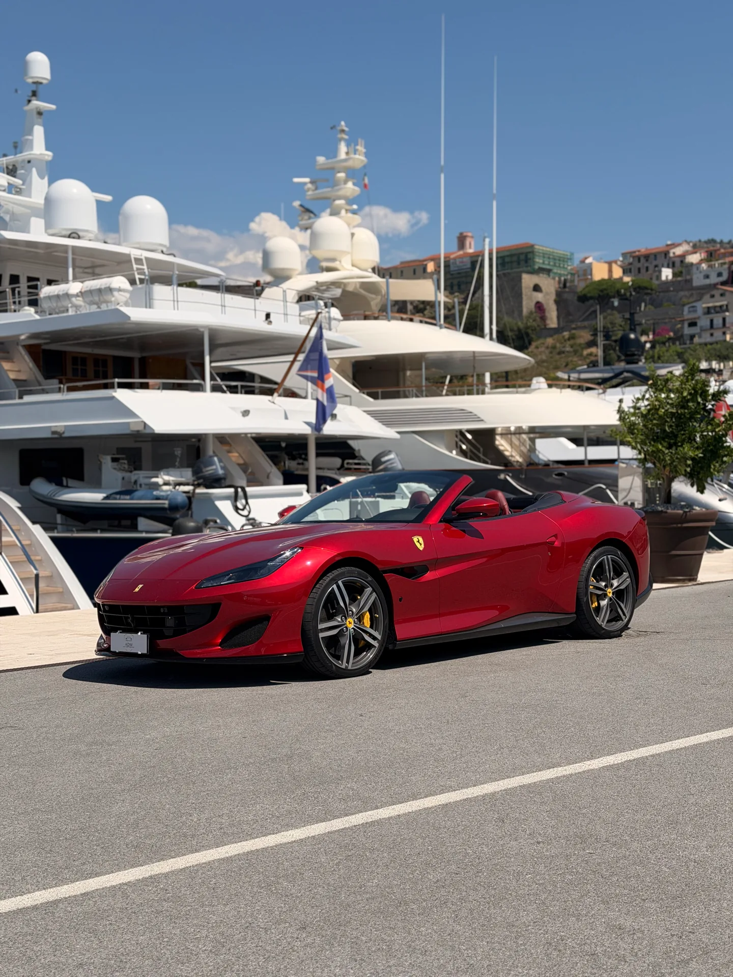 Red Ferrari Portofino with its roof open, viewed from the front three-quarter angle at a marina.
