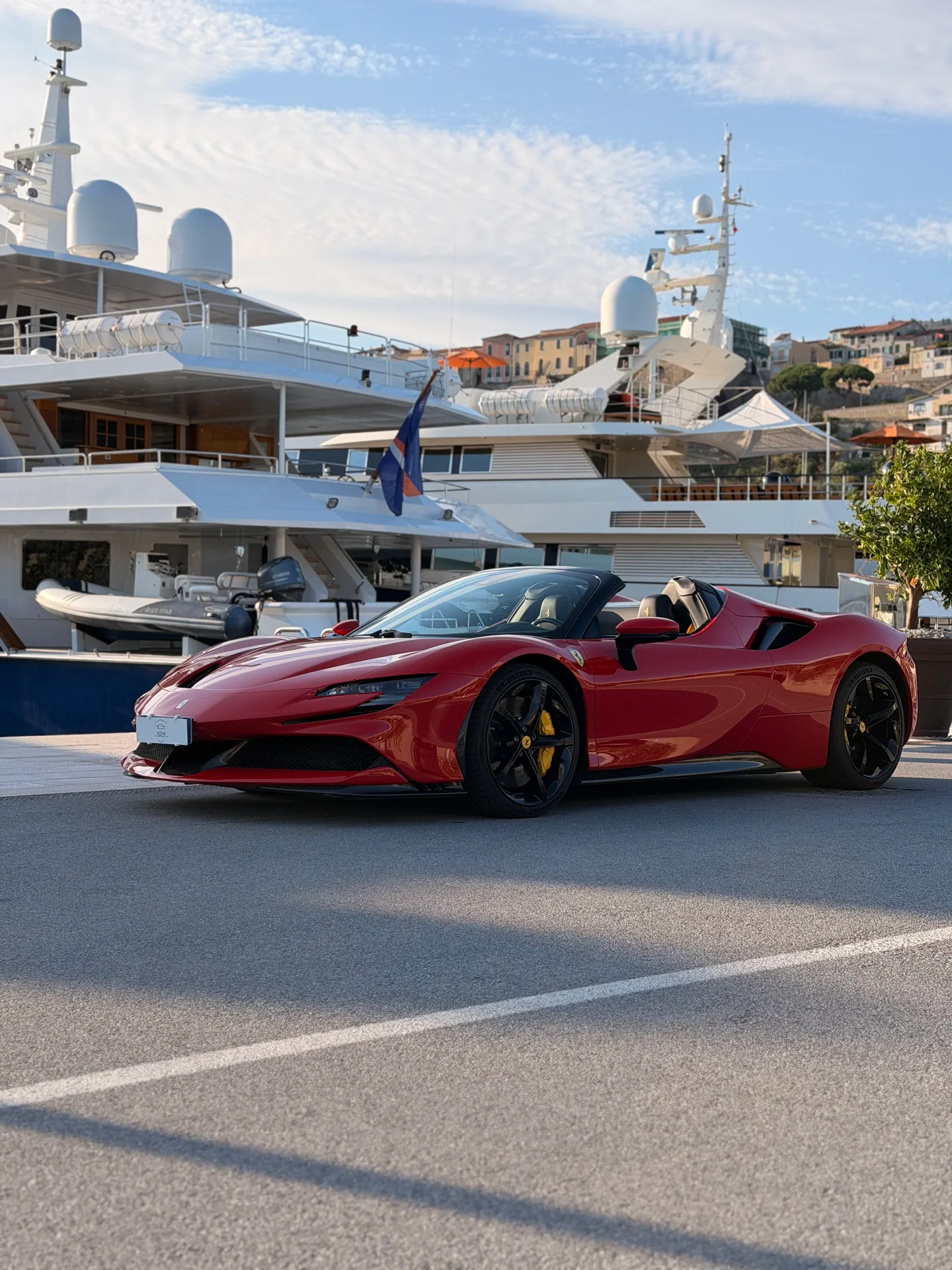 Red Ferrari SF90 with its roof open, seen from the front three-quarter angle at a marina.